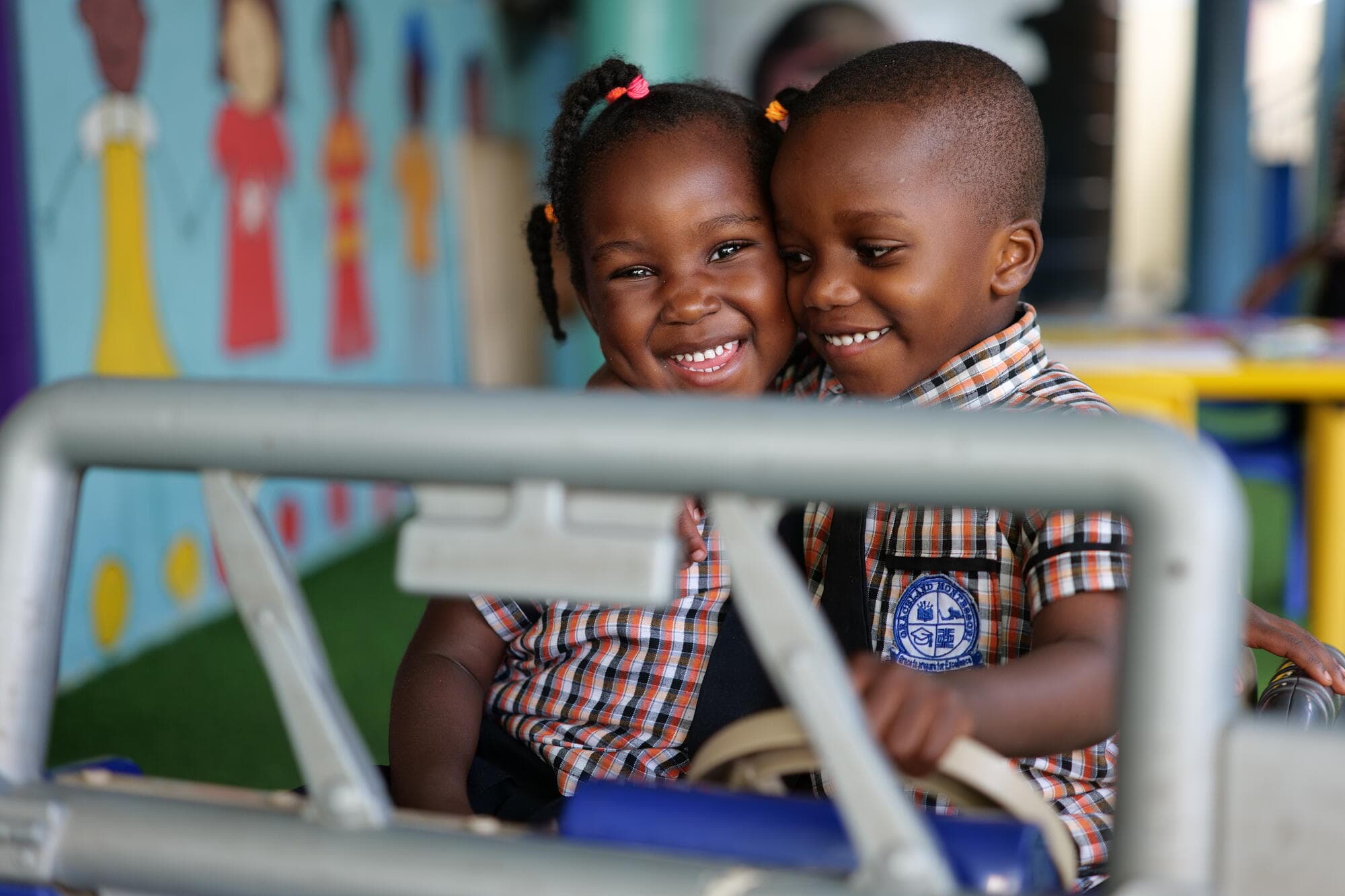 Two Graceland toddlers cheek to cheek and smiling together in a ride-on toy car