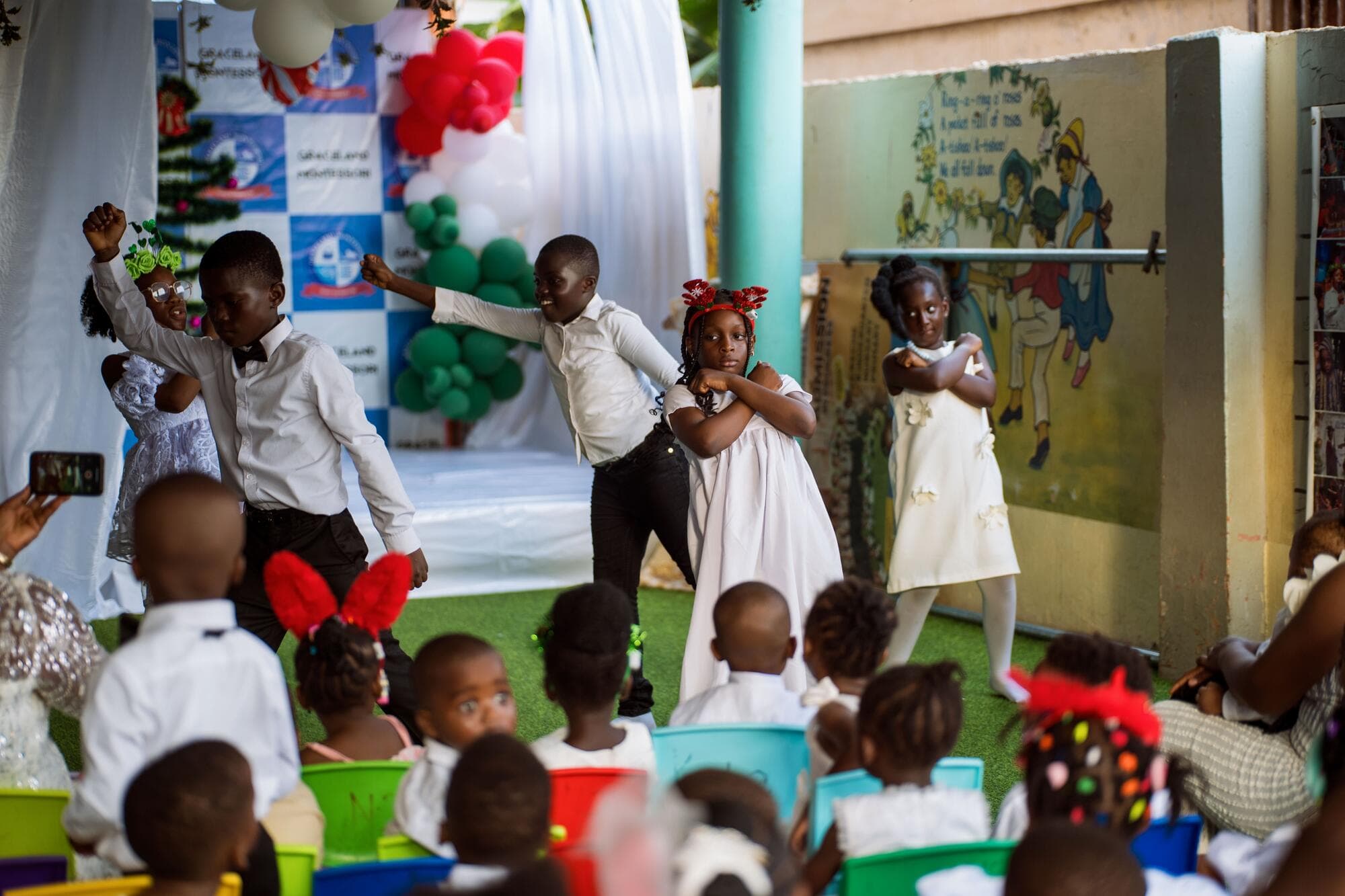 Pupils performing a nativity-style skit on a stage decorated with balloon arches