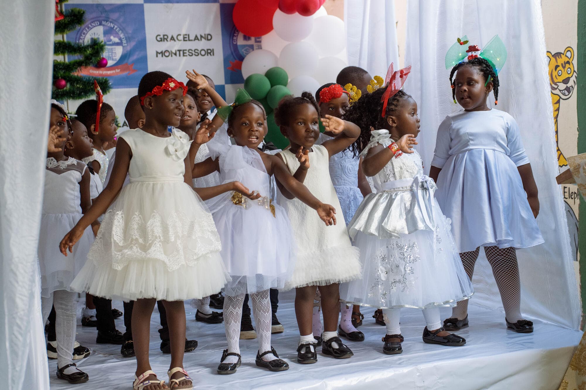 Graceland pupils dancing on stage in front of a Christmas-themed Graceland Montessori backdrop with balloon arches
