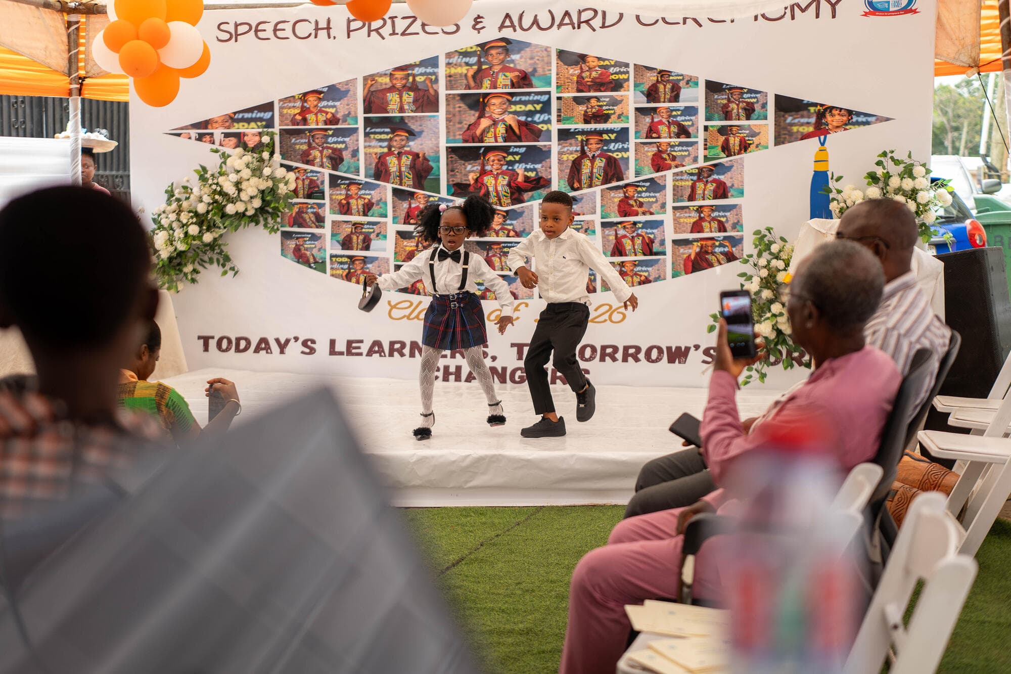 Two pupils running and jumping across the stage in front of the Speech, Prizes & Award Ceremony banner