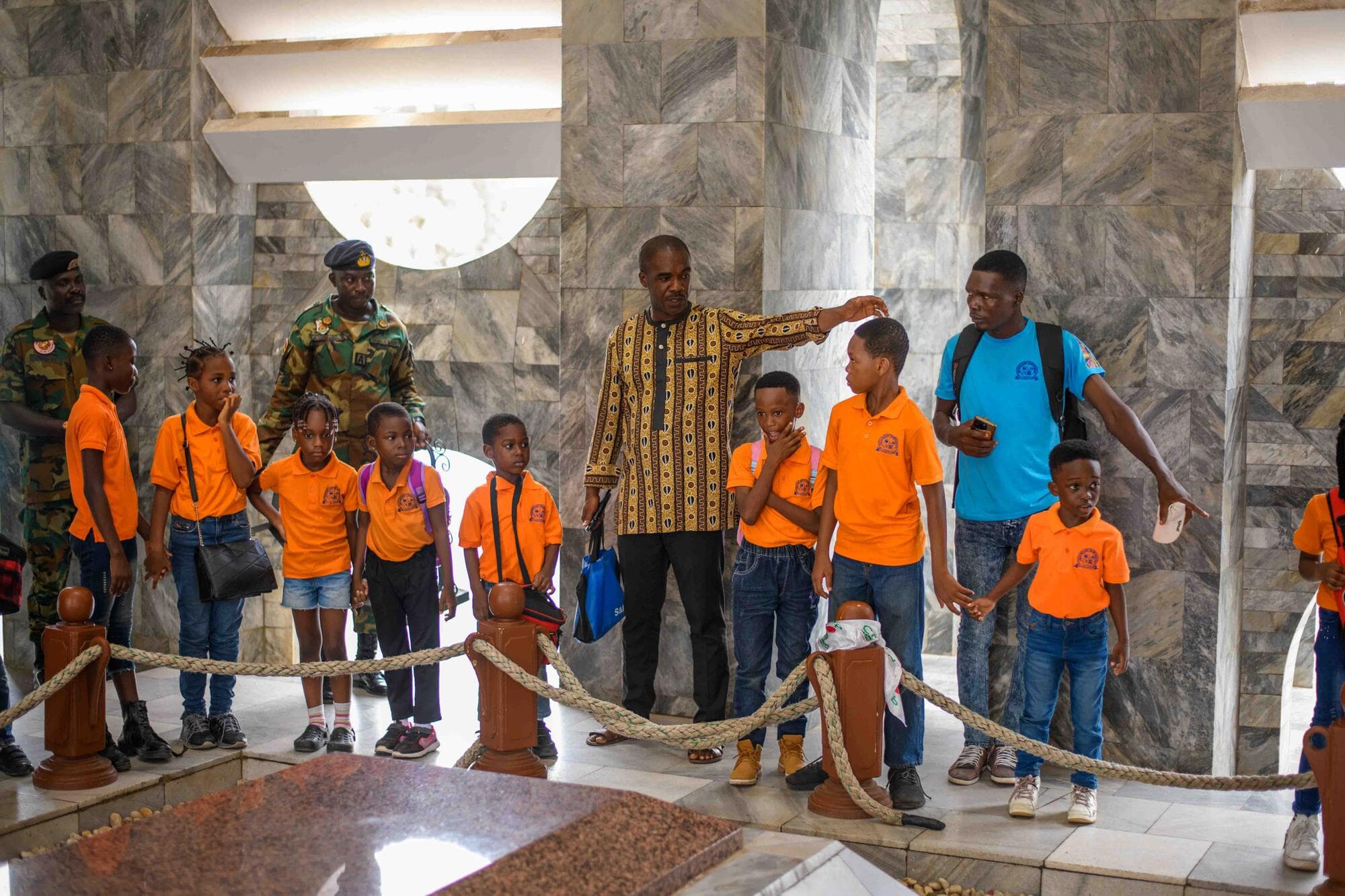 A guide playfully measuring a pupil's height beside the tomb