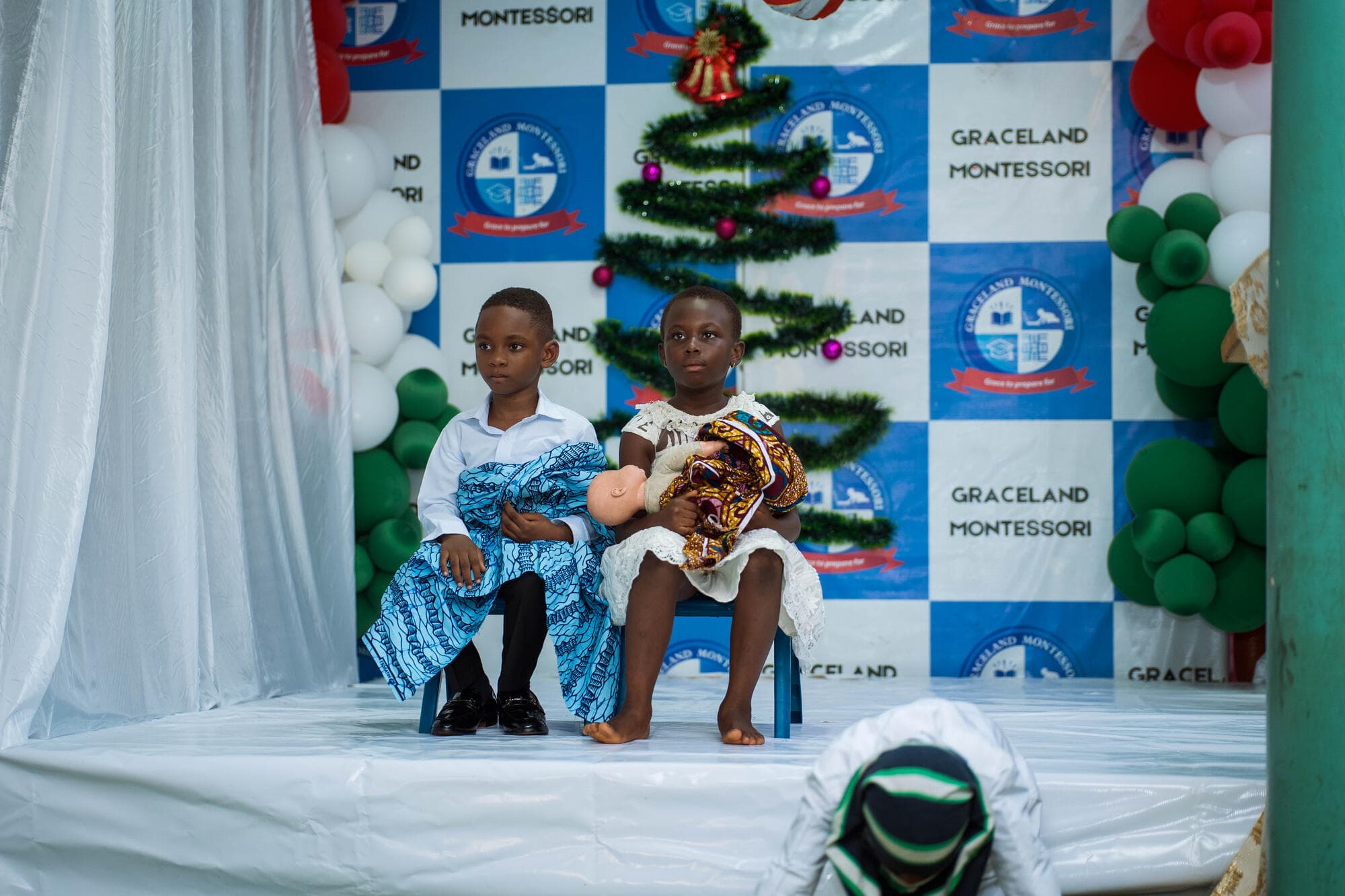 Two young pupils in kente-wrapped costumes holding baby dolls during the nativity performance