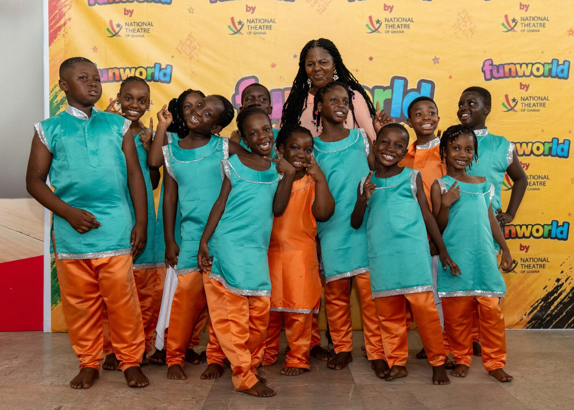 A group of Graceland pupils posing with a staff member in front of the FUNWORLD by National Theatre of Ghana backdrop