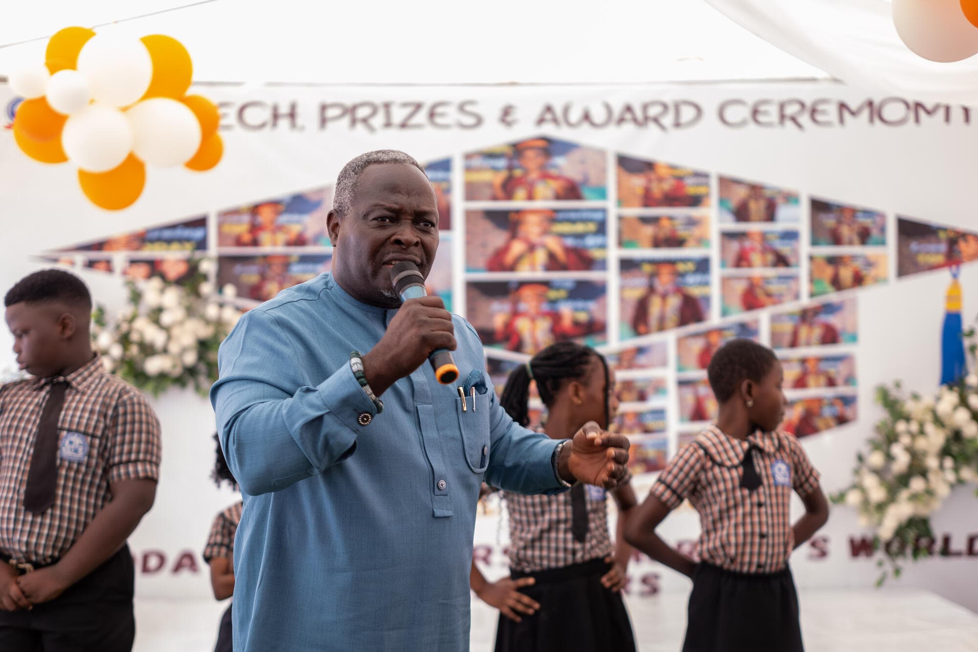 A staff member giving a speech at the podium while pupils dance in the background