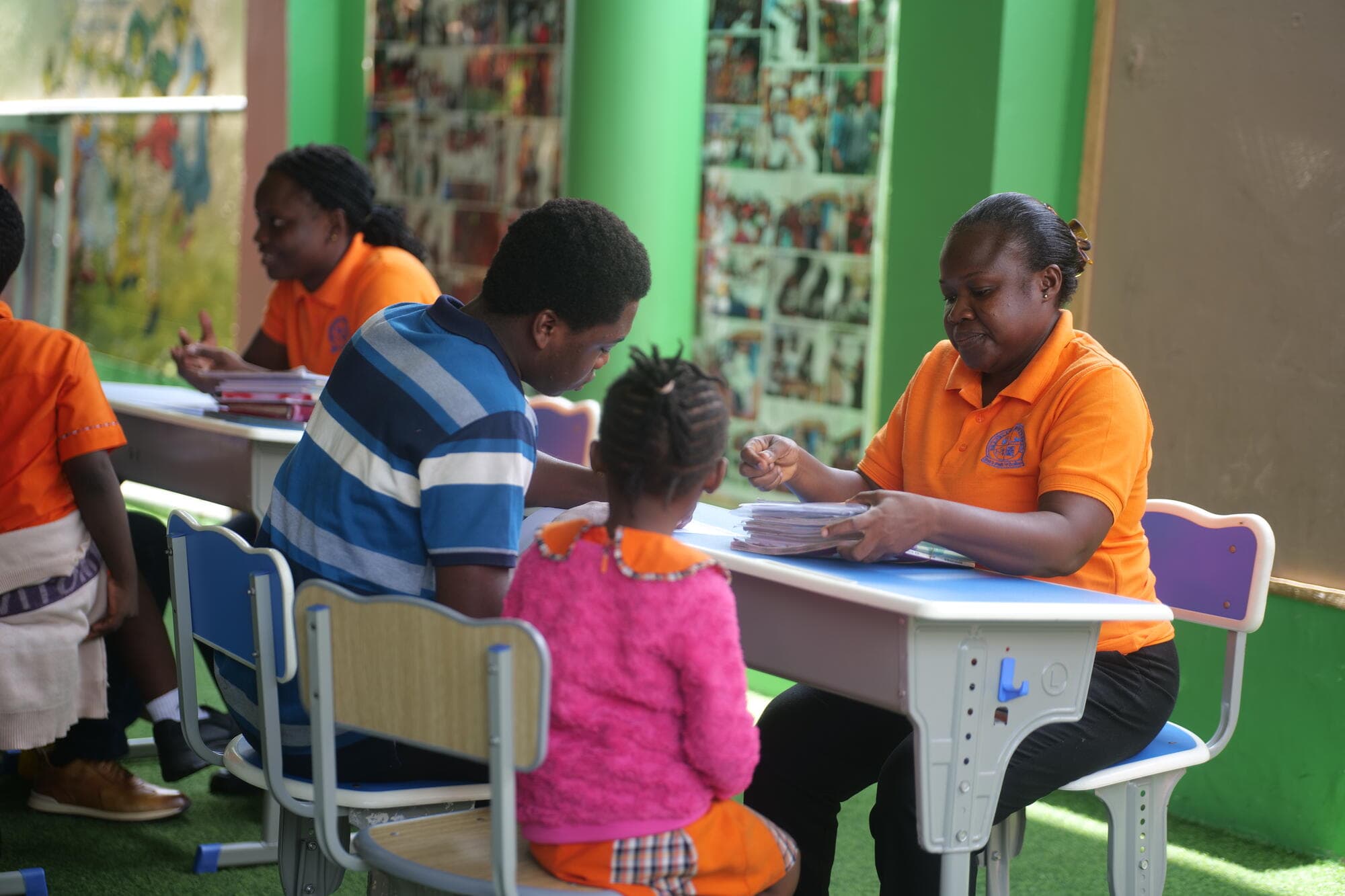 A teacher going through a stack of notebooks with a pupil and a parent nearby